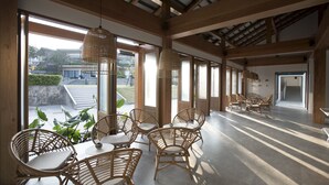 A spacious indoor area with large windows, wicker furniture, and a high ceiling with exposed beams. - Sook Hotel (Ranong)