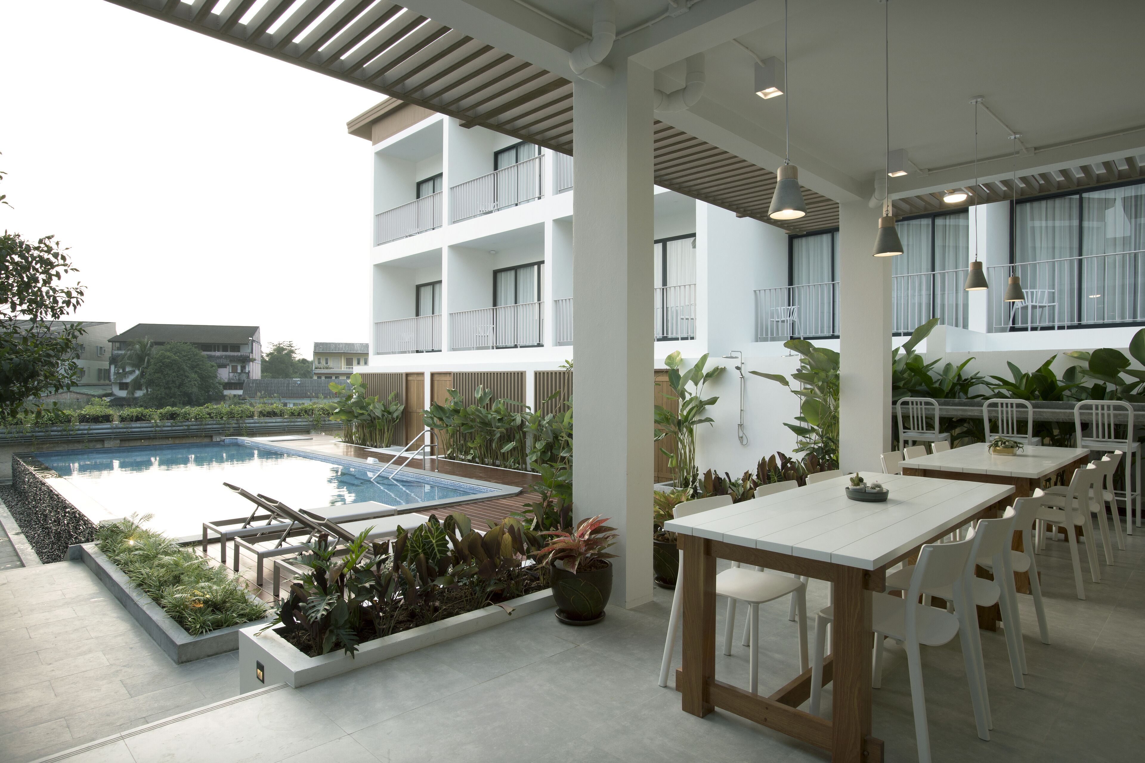A modern outdoor pool area with lounge chairs, a dining table with chairs, and potted plants.