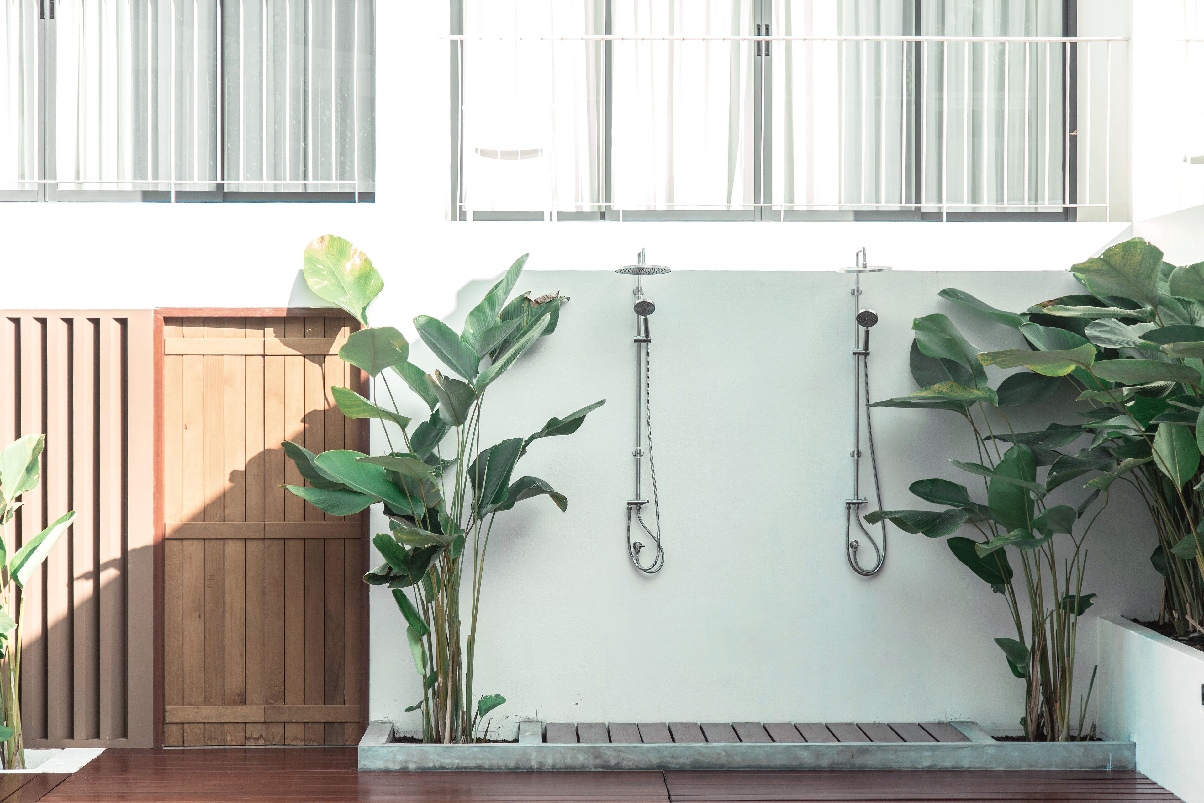 Una terraza de madera con un banco, plantas en macetas y una ducha empotrada en la pared.