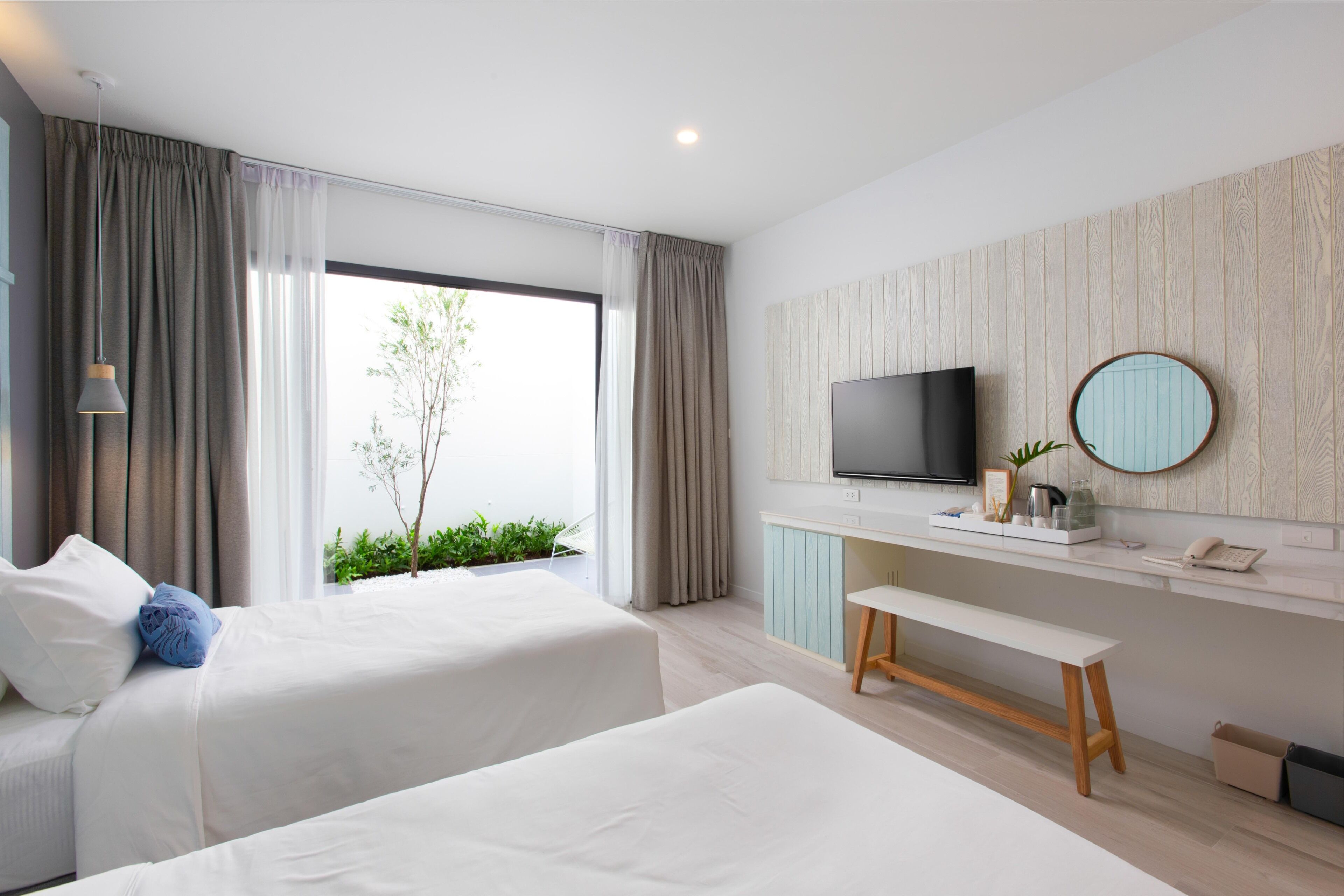 Una habitación de hotel moderna con dos camas, un televisor, un banco y vistas a zonas verdes.