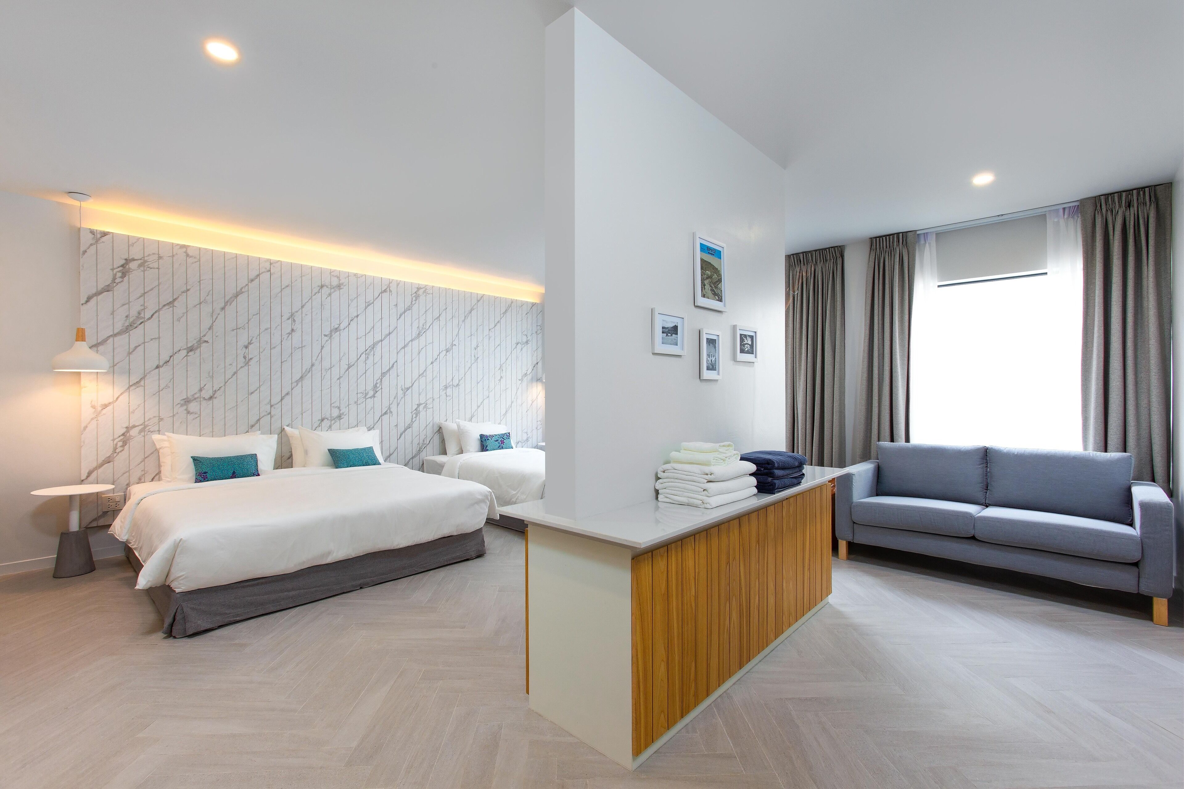 A modern hotel room with a large bed, a sofa, a wooden desk, and a marble-patterned wall.