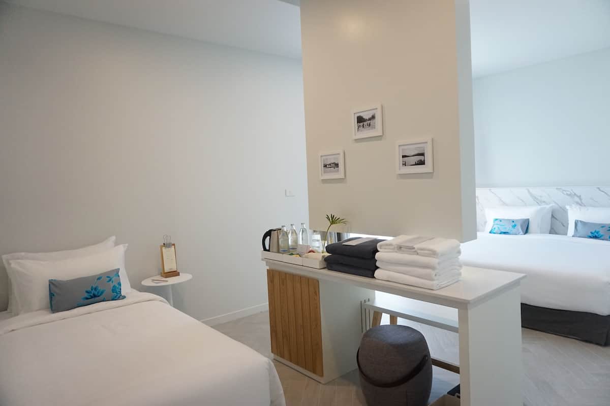 Una habitación de hotel moderna con dos camas, una mesita con toallas, una mesita de noche y cuadros en la pared.