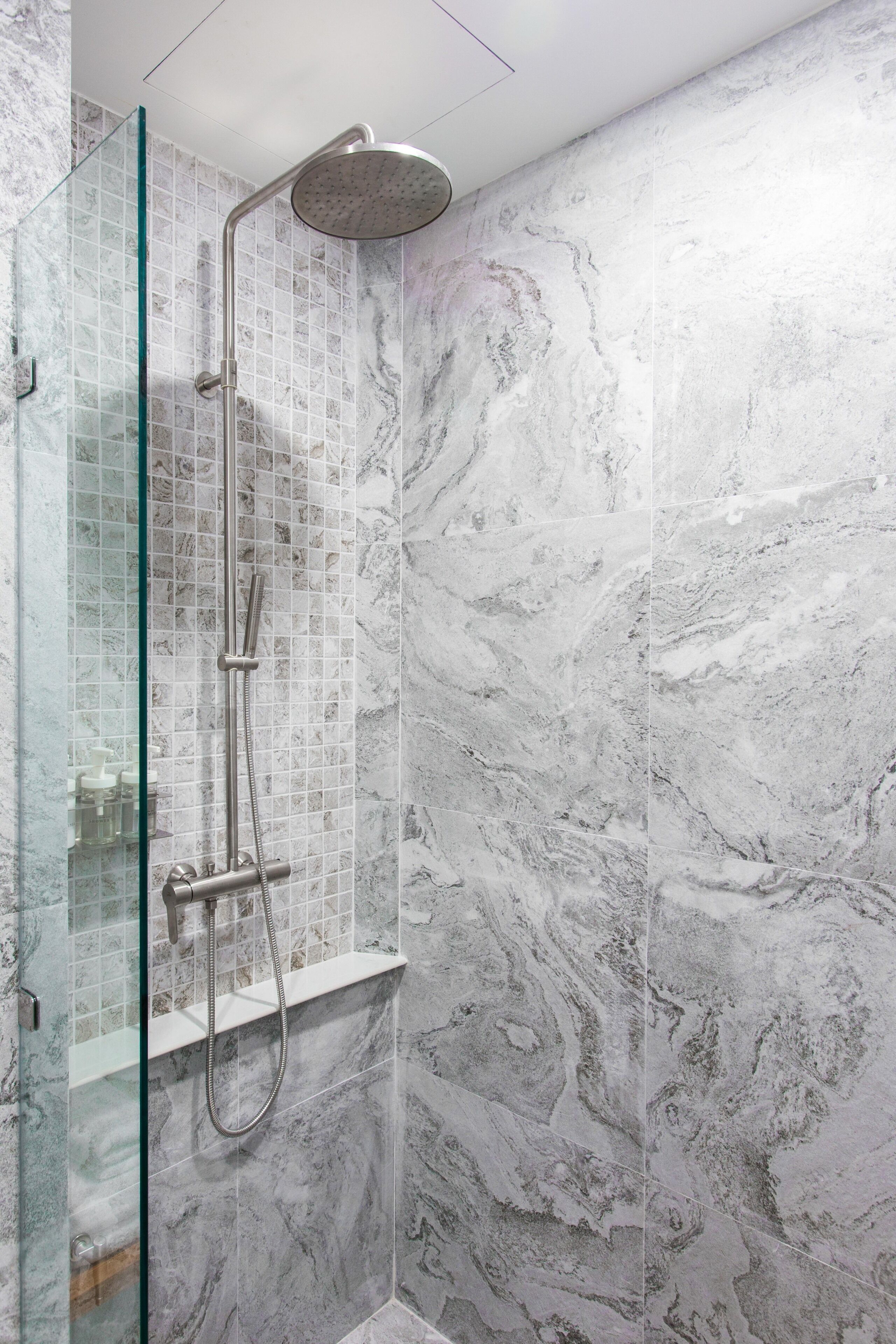 A modern shower with a glass enclosure, a handheld showerhead, and a wall-mounted control panel.
