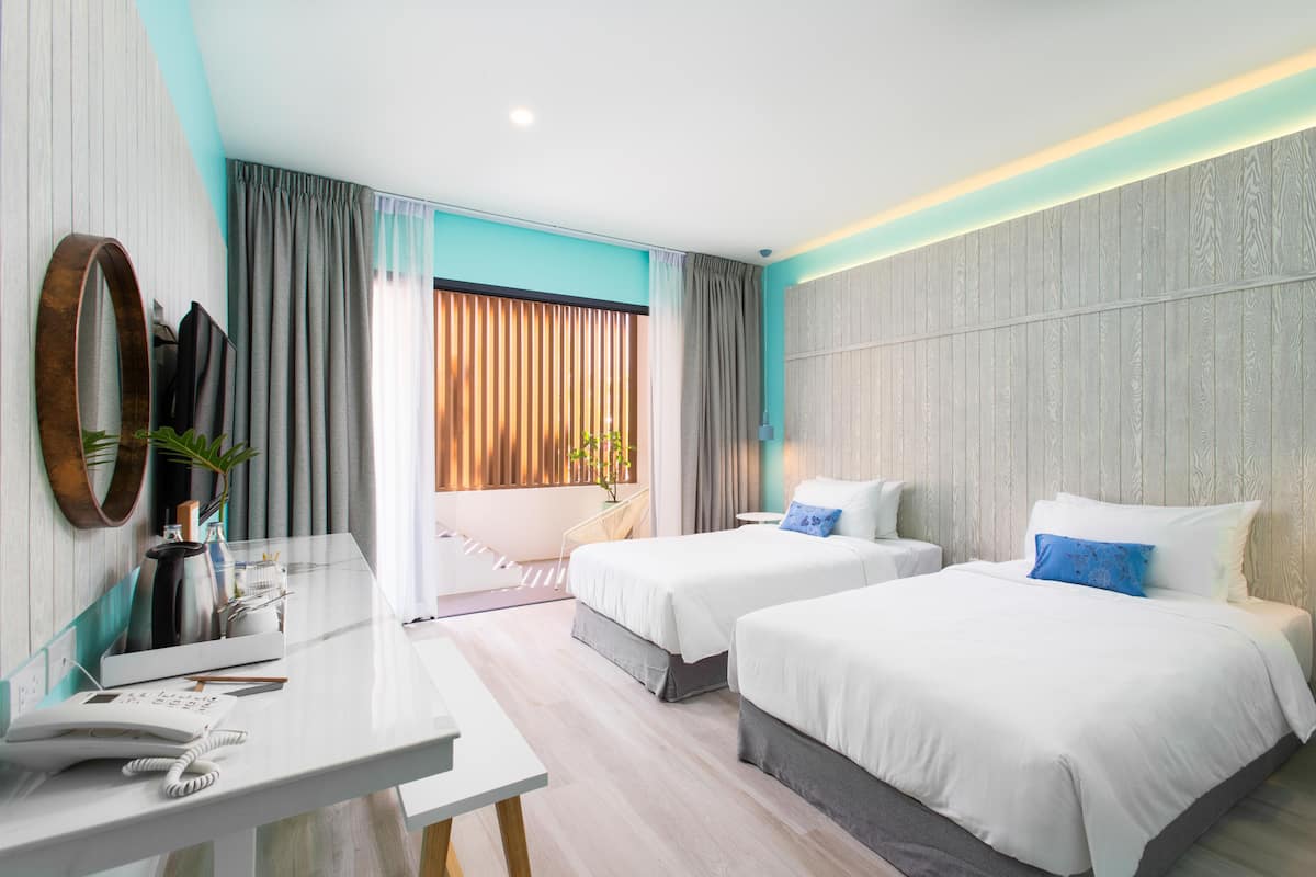 A hotel room with two beds, a desk, a mirror, and a window with curtains.