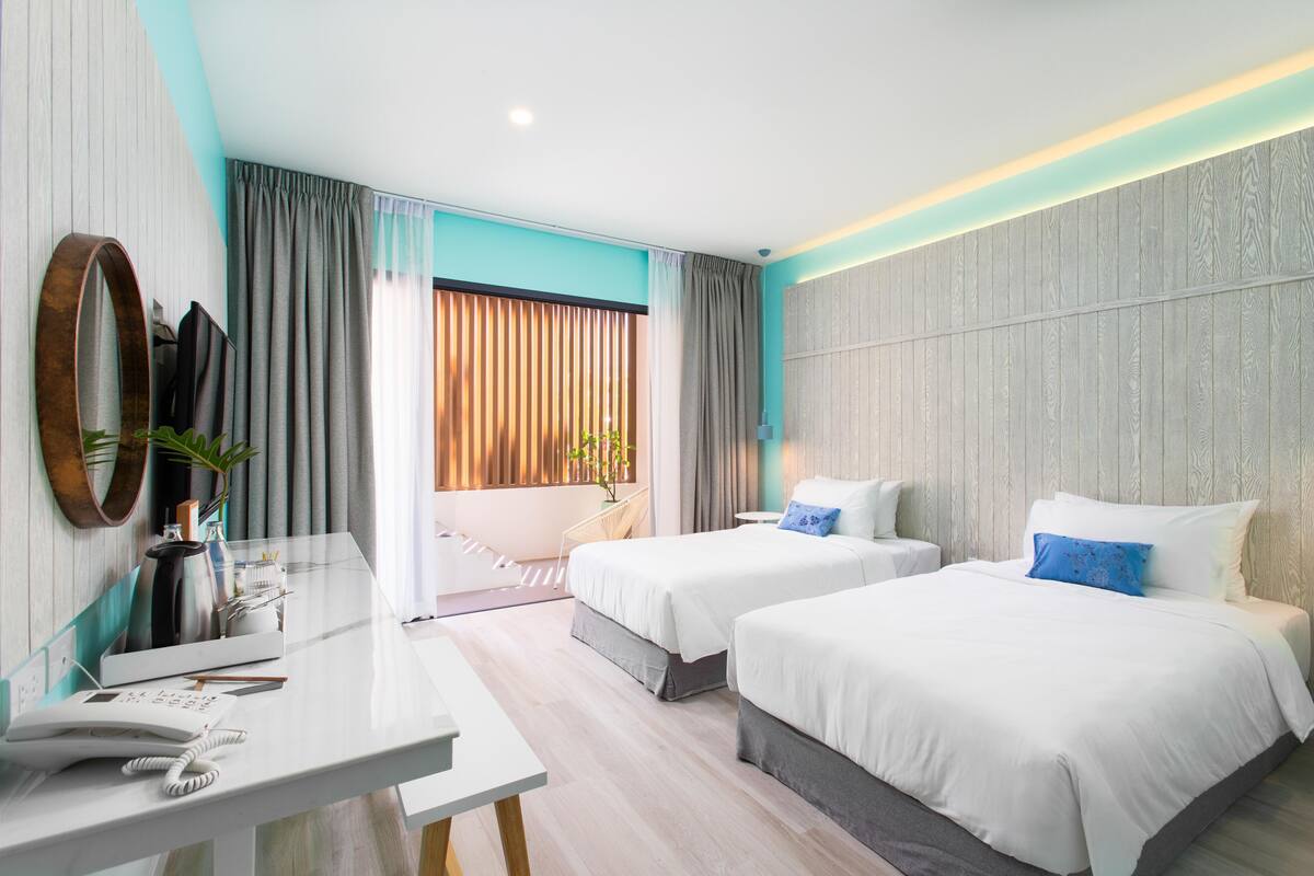 Habitación de hotel con dos camas, un escritorio, un teléfono, un espejo y vista al exterior.
