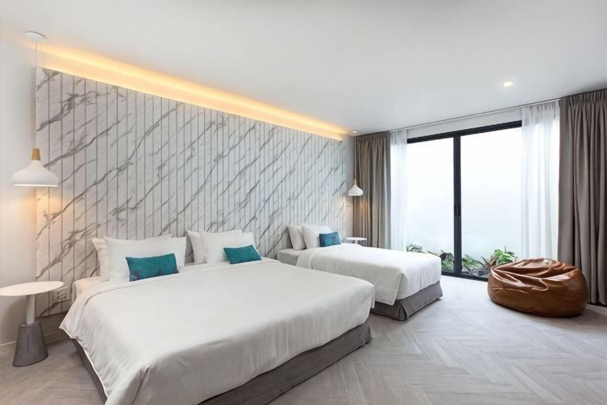 Una habitación de hotel moderna con dos camas, un ventanal grande y un sillón informal.
