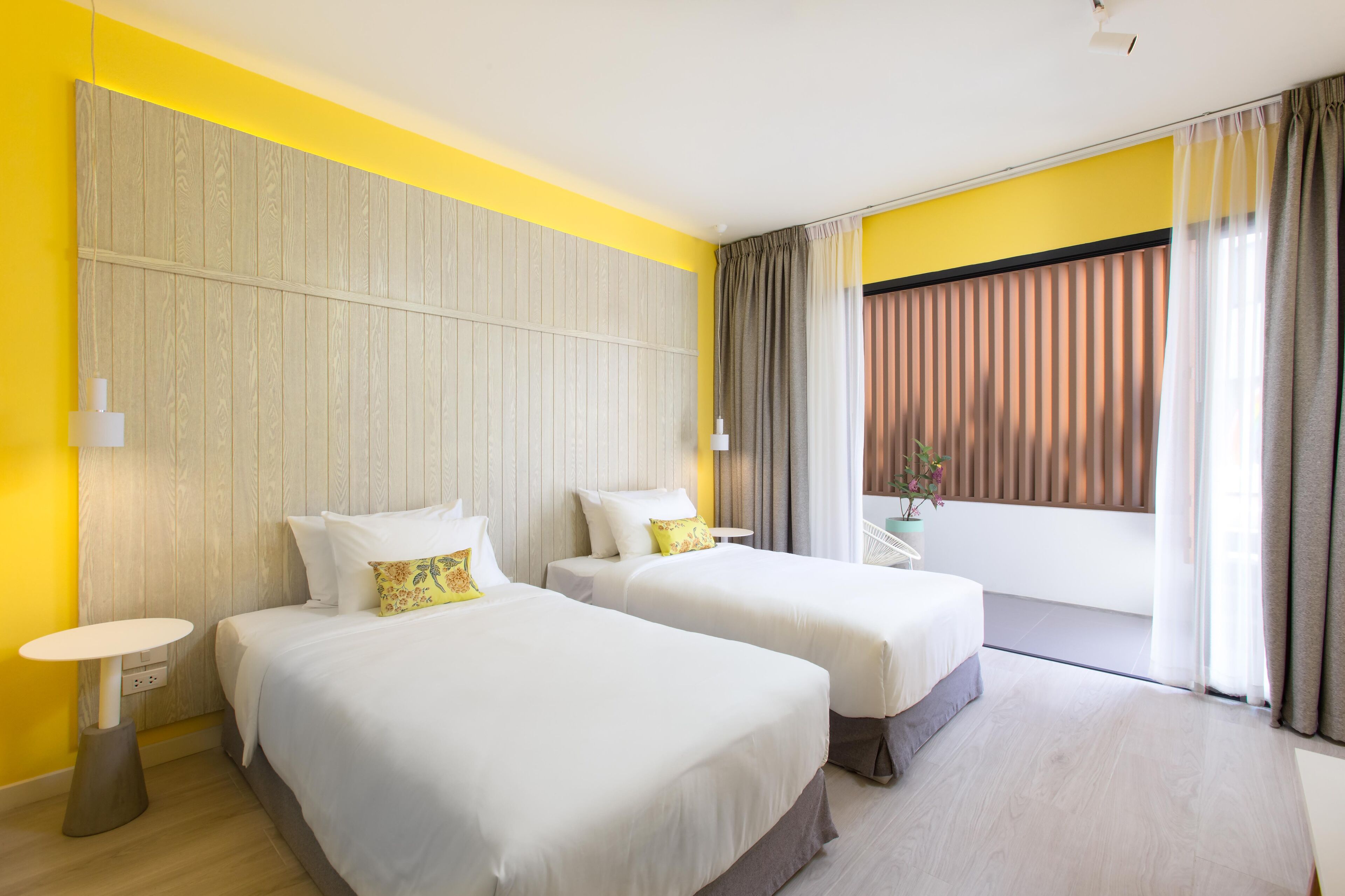 A hotel room with two beds, a small table, and a balcony with curtains.