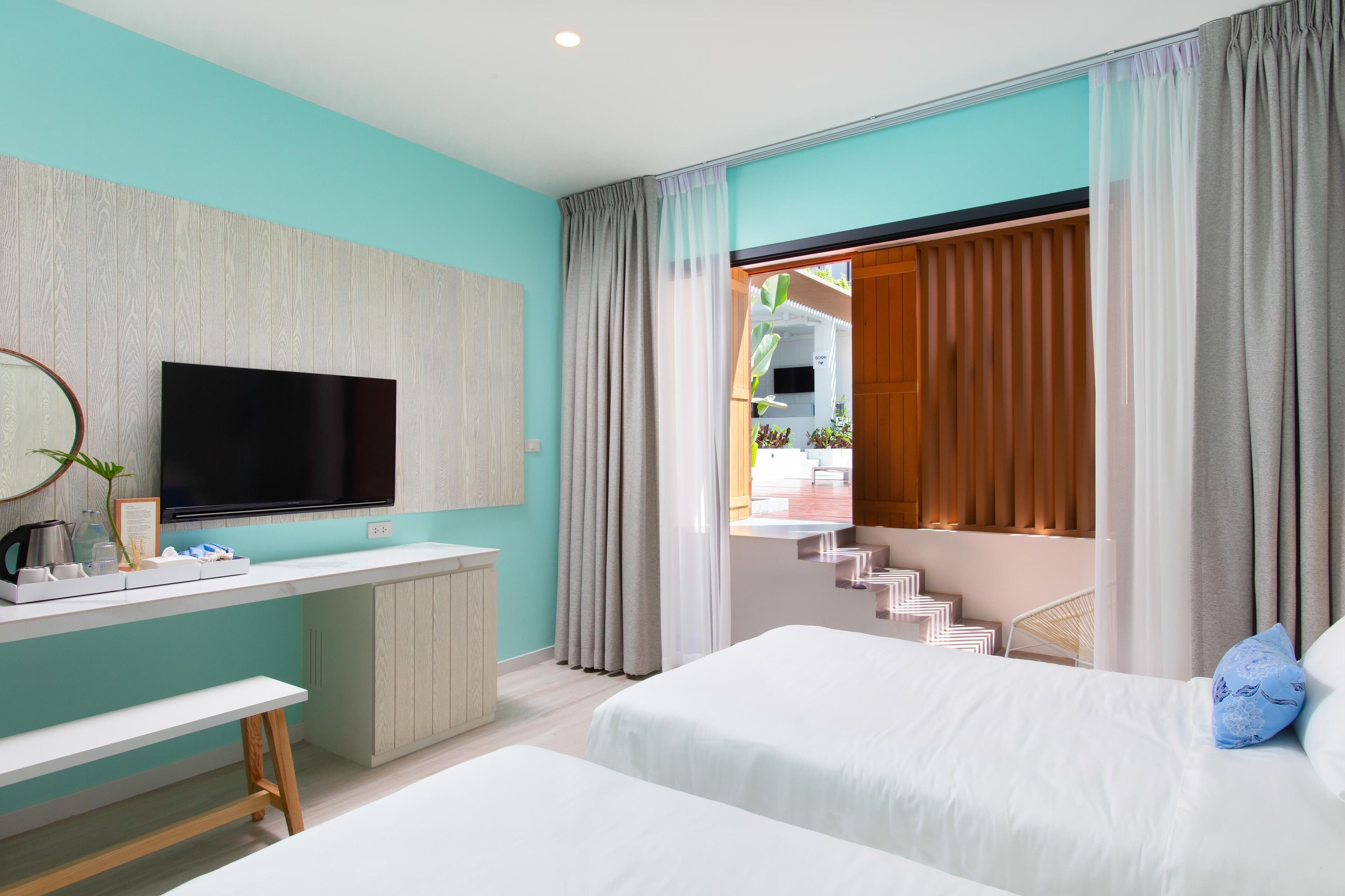 A modern hotel room with a large flat-screen TV, a desk with a coffee maker, and a bench.