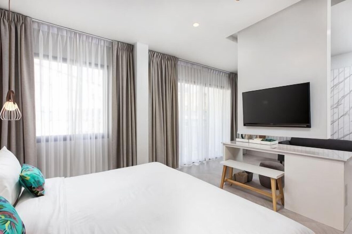Una habitación de hotel moderna con una cama grande, un televisor montado en la pared y un escritorio con una silla.