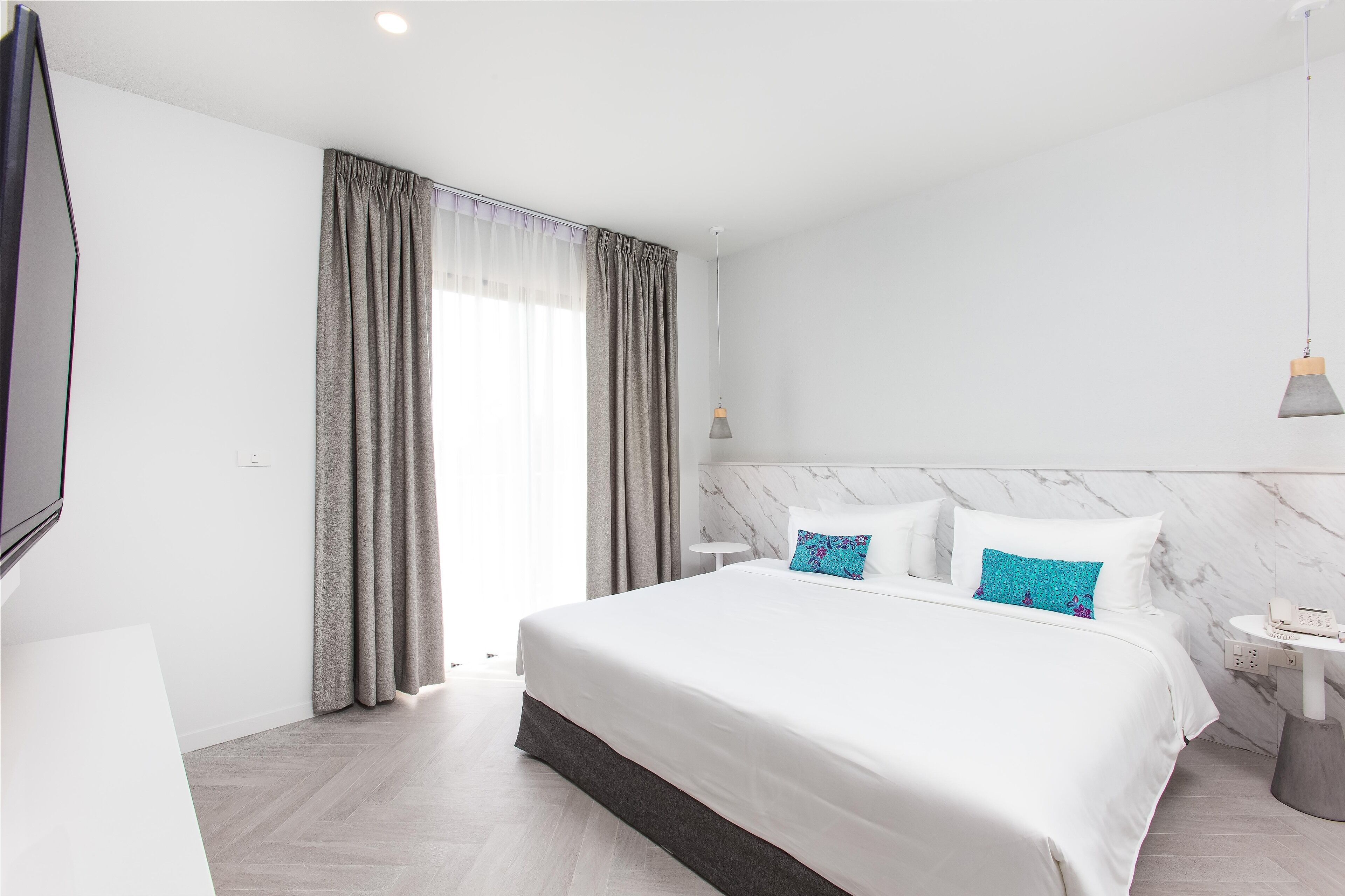 A modern hotel room with a large bed, a bedside table with a phone, and a marble headboard.