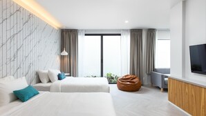 A modern hotel room with two beds, a bean bag chair, a TV, and a large window with curtains. - Sook Hotel (Ranong)
