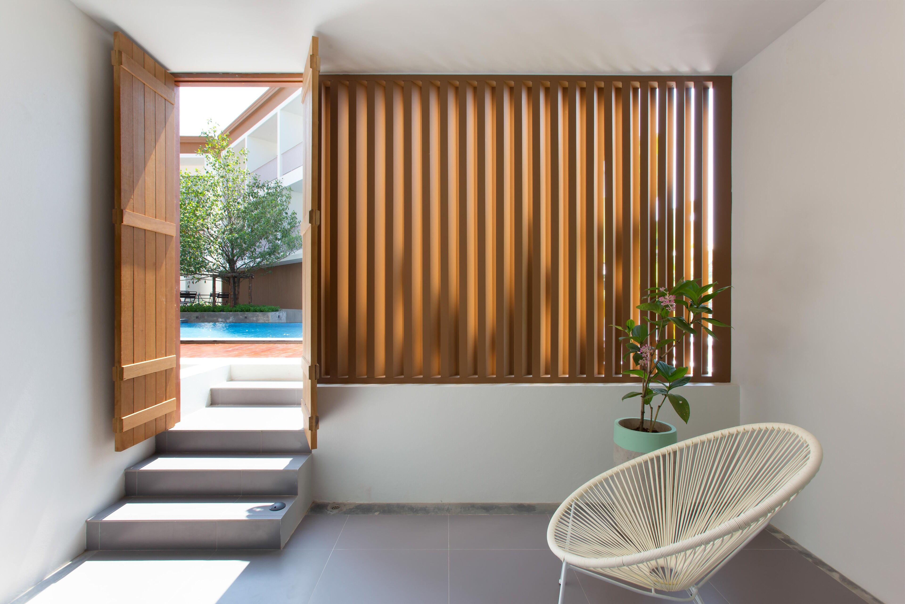 A modern interior with a staircase leading to an outdoor area, a white wicker chair, and a wooden slatted wall.