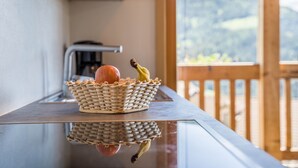 Un panier en osier contenant une pomme et une banane, posé sur une surface réfléchissante, avec en arrière-plan une terrasse en bois et des montagnes.