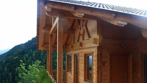 Une cabane en bois dotée d’un balcon, de grandes fenêtres et offrant une vue sur une montagne boisée.