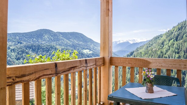 Un balcon en bois avec une table et une chaise, donnant sur un paysage montagneux.