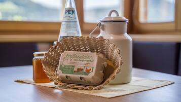 A table with a woven basket containing a package of eggs, a bottle of PEJ beer, and a ceramic pitcher.