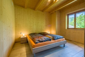A wooden-paneled room with a bed, a nightstand, and a window with a view of greenery. - Charming Cottage Eckgenn with Wi-Fi, Mountain View, Garden & Terrace (Laurein)