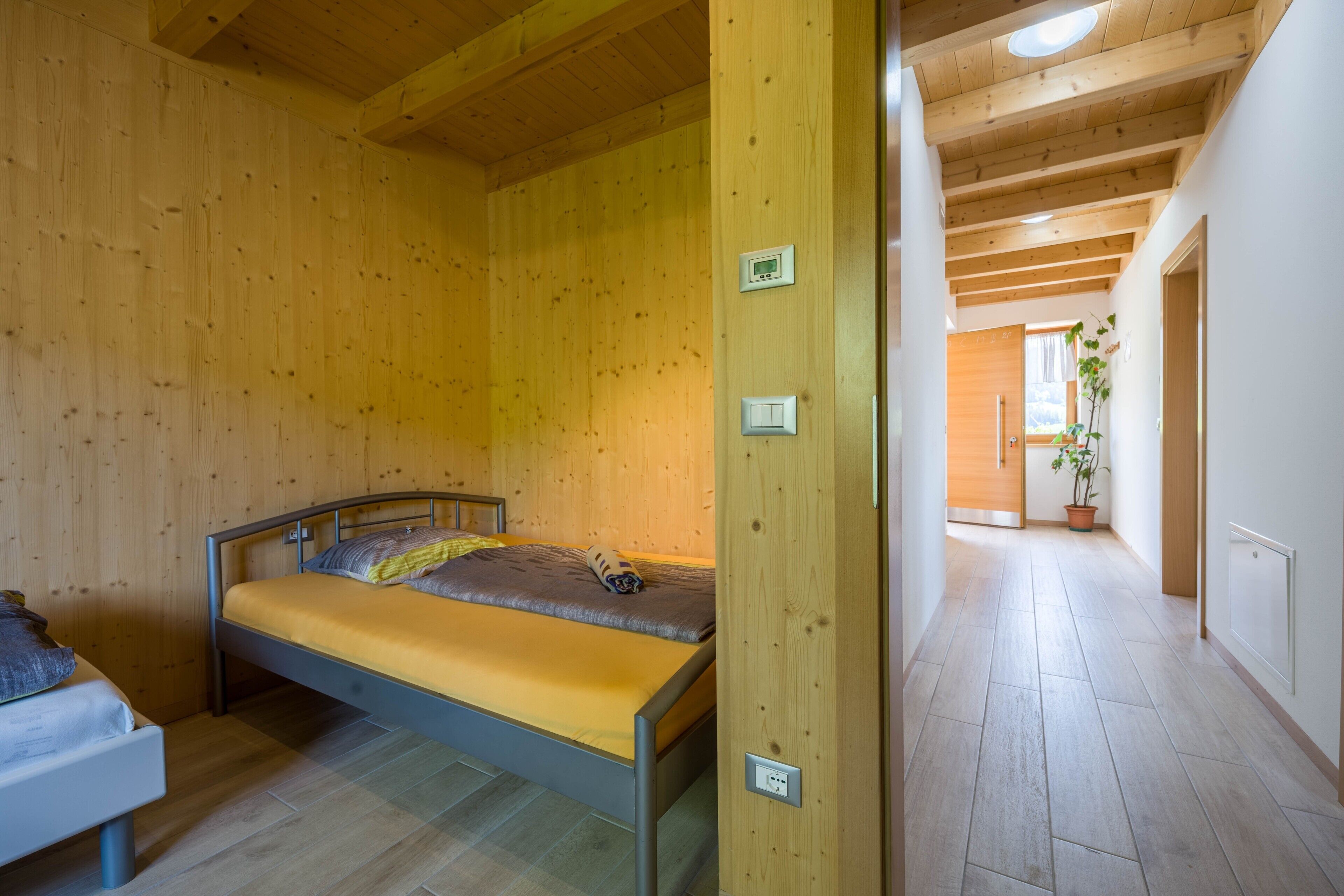 A wooden-paneled room with a bed, a bedside table, and a potted plant.