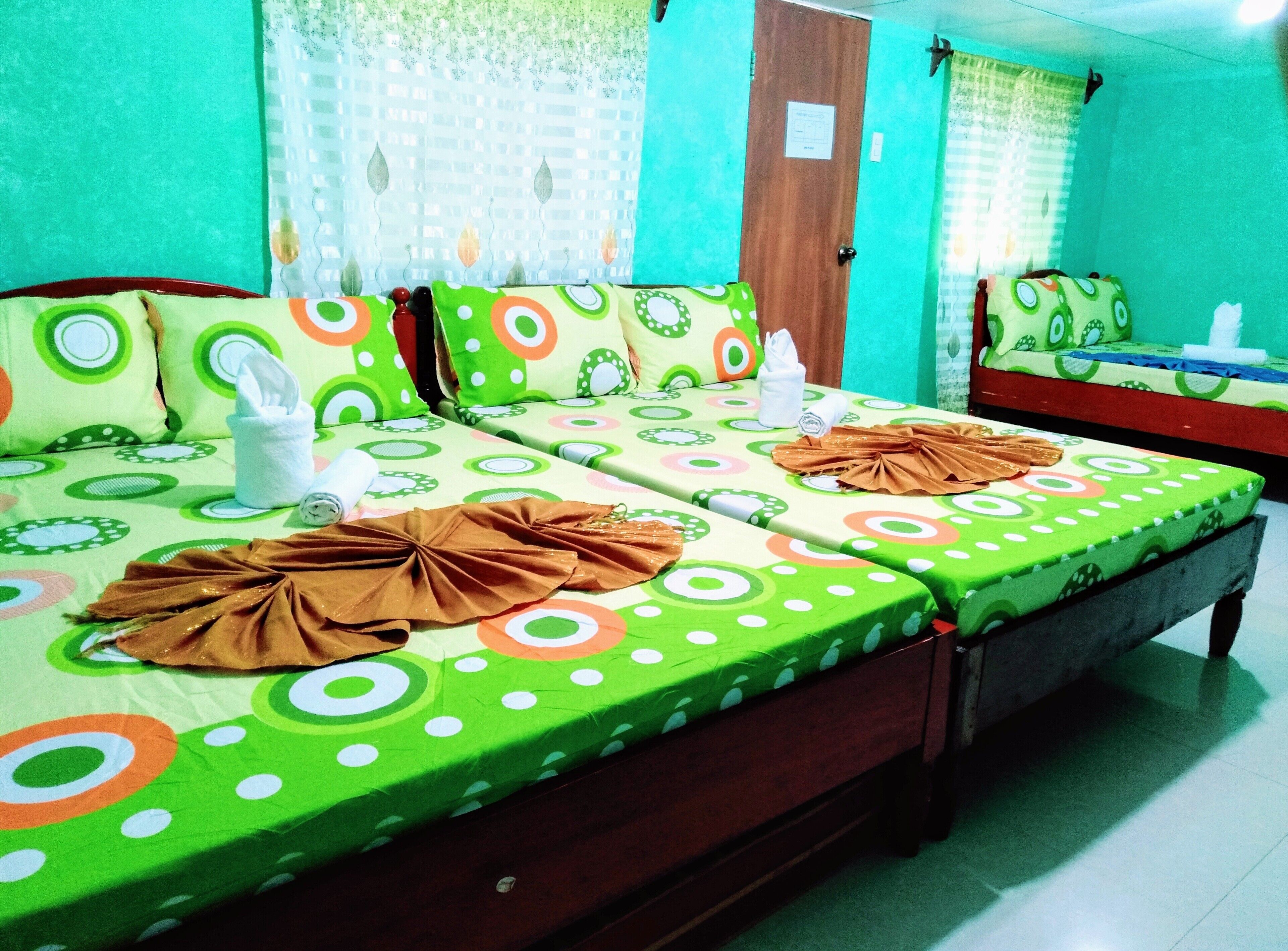 A room with two beds, each with green bedsheets featuring circular patterns. There are towels and a brown cloth on the beds.