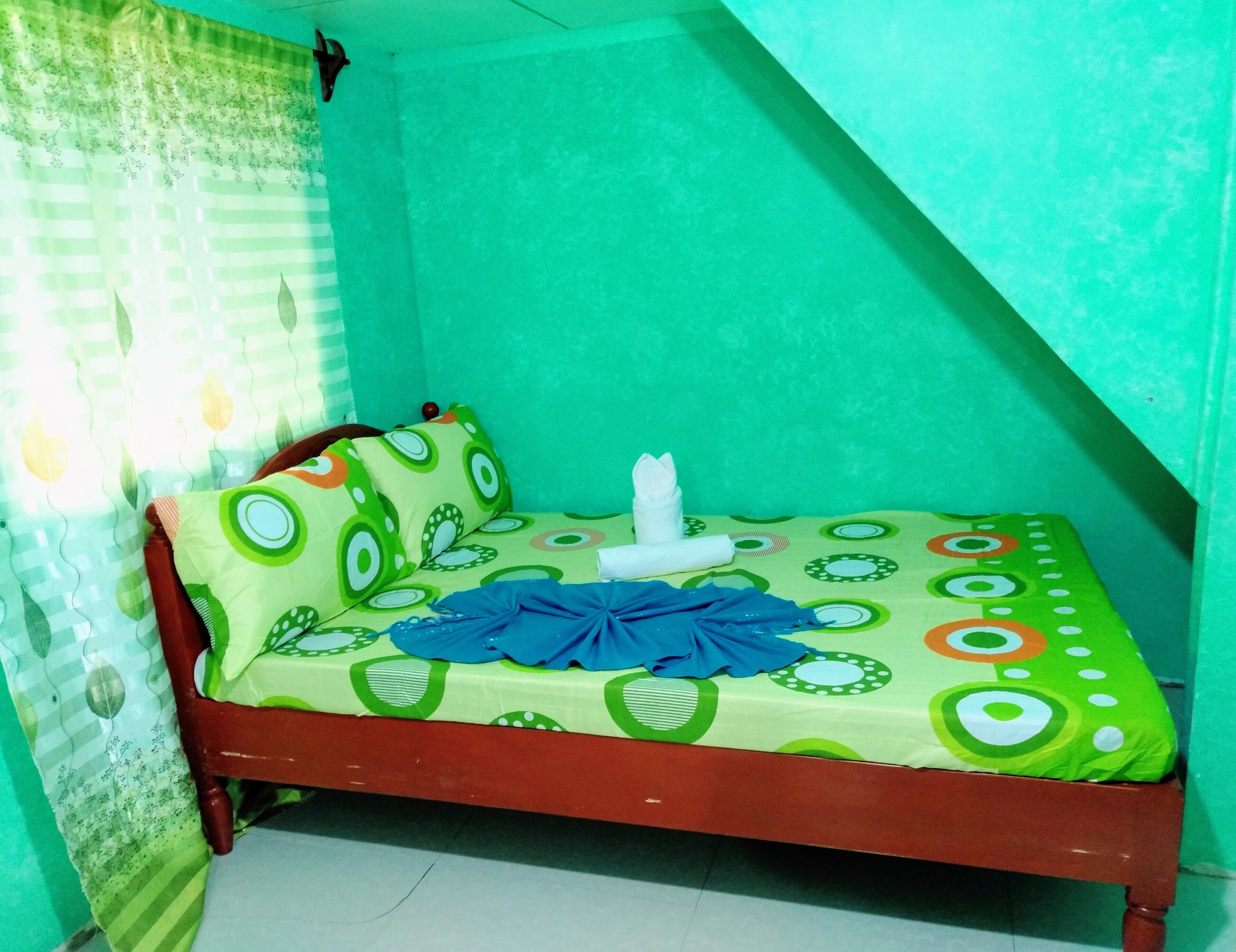 Una habitación pequeña con una cama individual, pared verde y colcha estampada.