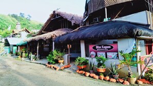 Un bâtiment traditionnel avec un toit de chaume, une enseigne indiquant « Blue Lagoon Sharmar », et des plantes en pot devant l’entrée.