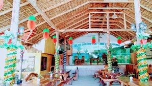 Un restaurant à l’intérieur rustique, avec des murs en bois, un plafond en bambou et une enseigne indiquant « BLUE LAGOON, RESTAURANT ET CENTRE DE BIEN-ÊTRE ».