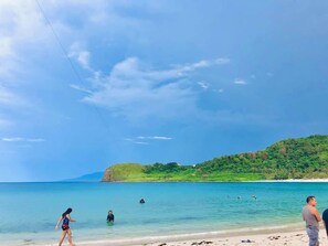 A beach with clear water, a sandy shore, and a green hill in the background. - Blue Lagoon Inn and Restaurant (Pagudpud)