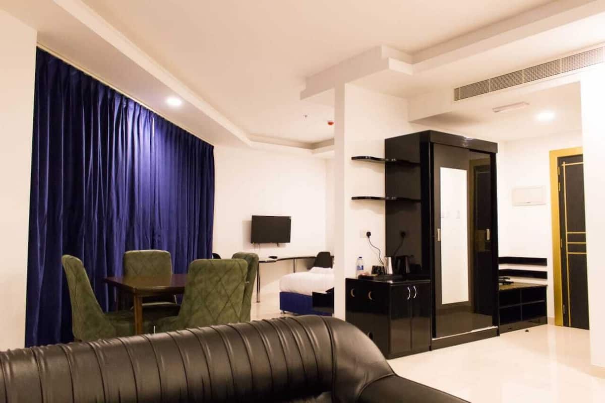 A modern hotel room with a living area featuring a sofa, a dining table with chairs, a television, and a wardrobe.