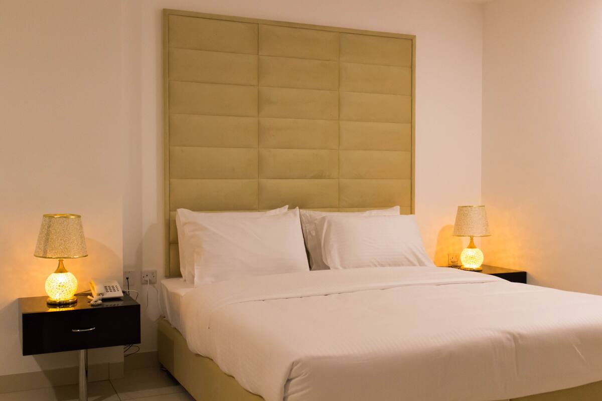 A neatly made bed with white linens and a headboard, two bedside tables with lamps, and a telephone on one of the tables.