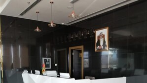 A modern reception desk with a glass partition, a flag, and a framed portrait on the wall. - Parkside Plaza Hotel - Muscat (Muscat)