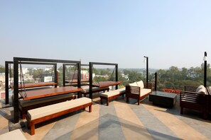 Une terrasse sur le toit, aménagée avec des bancs en bois, un canapé et une table, et offrant une vue sur le paysage urbain.