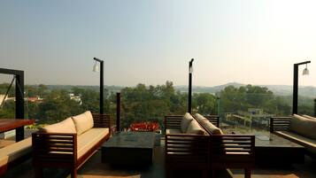 A rooftop terrace with a sofa, chairs, and a table, offering a view of a cityscape.