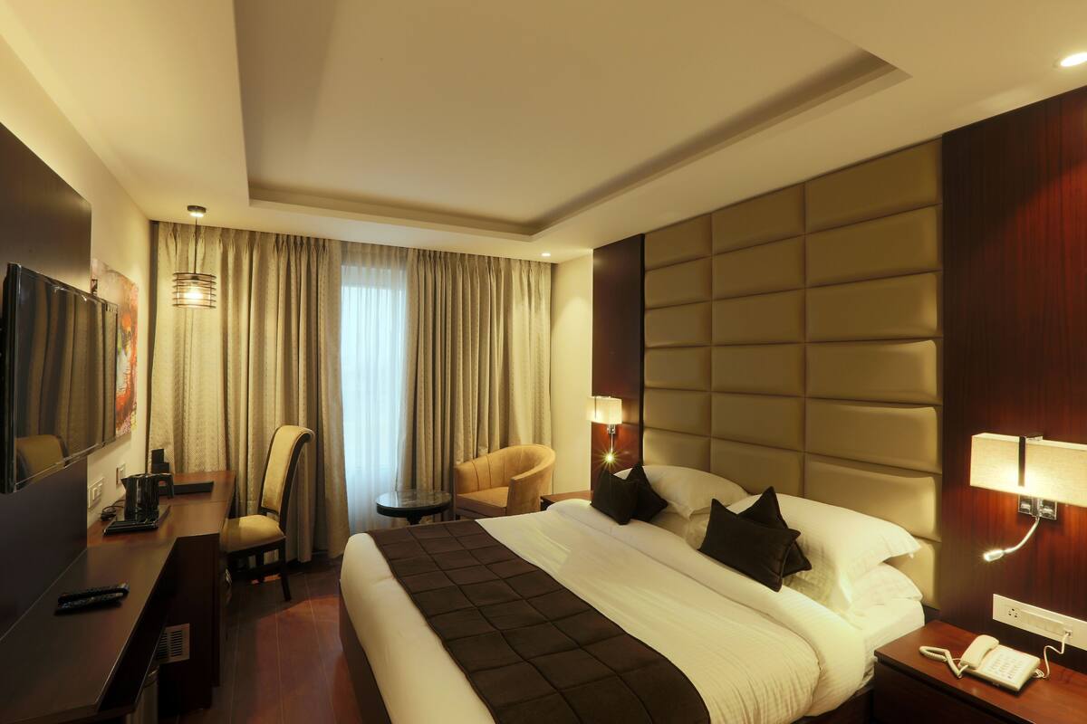 Una habitación de hotel con cama, escritorio, silla, televisor y lámpara.