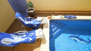 En liten inomhuspool med blå kakelplattor på botten, ett bubbelbad och en solstol.