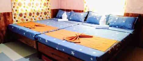 Una cama doble con una colcha azul y naranja estampada con estrellas, dos almohadas con diseños de estrellas y una cortina amarilla con lunares.