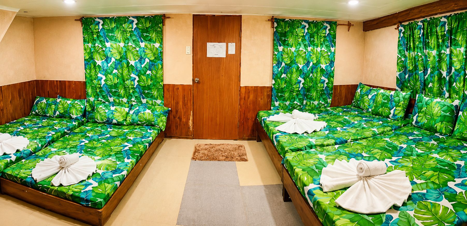A hotel room with two beds, each with a tropical leaf pattern bedspread and a towel on the bed.