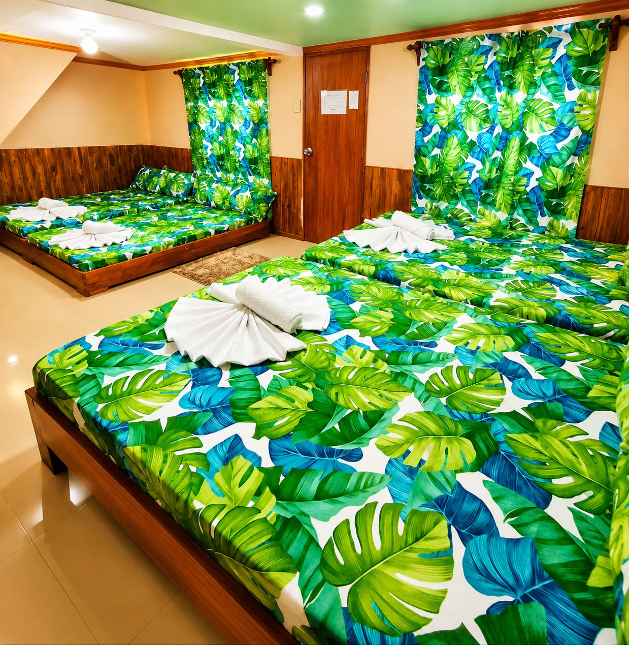 A hotel room with two beds, each with a tropical leaf-patterned bedspread and neatly folded towels.