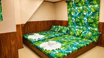 Una habitación con una cama que presenta un diseño de hojas tropicales, paneles de madera y una toalla blanca sobre la cama.