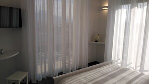 Ein Hotelzimmer mit einem Bett, einem kleinen weißen Schreibtisch, einem Regal mit einem Globus und transparenten Vorhängen.