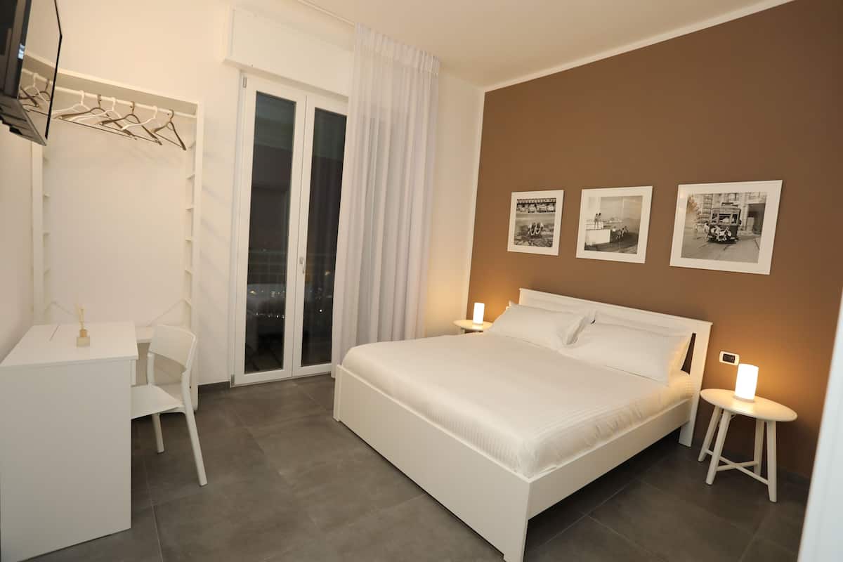 A bedroom with a bed, bedside tables, a desk, and a chair. There are three framed pictures on the wall.