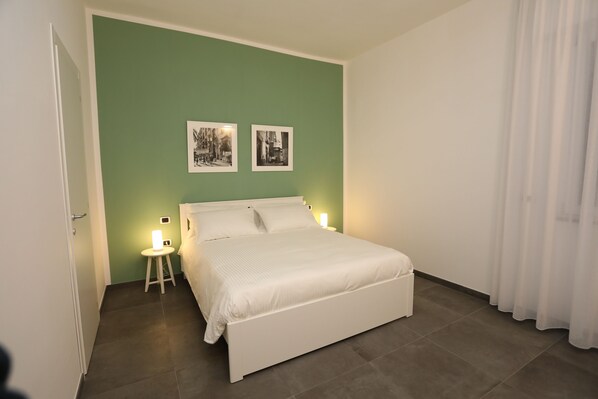 A bedroom with a bed, two bedside tables with lamps, a green wall, and two framed pictures. - Delia Rooms & Gallery (Naples)