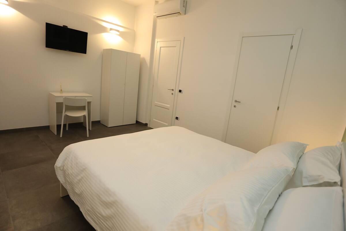 A bedroom with a bed, a desk, a chair, and two doors.