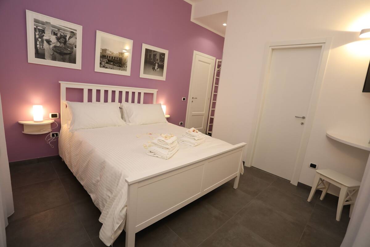 A neatly arranged bedroom with a bed, bedside tables, and a small stool.