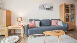 A living room with a grey sofa, wooden side tables, a white pet bed, a wooden cabinet, and a painting on the wall. - Apartment Bike & Ski Kappe at the bike park / ski lift - Apartment Bike & Ski Kappe (Winterberg)