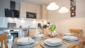 A modern kitchen with stainless steel appliances, a dining table set for six with placemats, and a vase with flowers. - Apartment Bike & Ski Kappe at the bike park / ski lift - Apartment Bike & Ski Kappe (Winterberg)