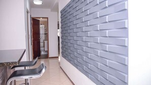 Un couloir avec un mur en briques grises, une porte donnant sur une salle de bain et deux chaises.