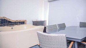 Une pièce avec une grande baignoire, une table avec des chaises et un petit meuble.