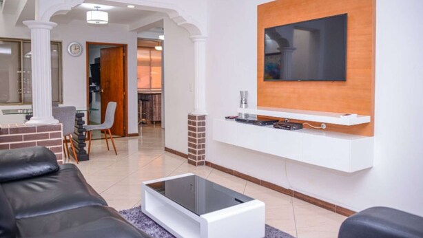 Un salon moderne avec un téléviseur à écran plat fixé sur un panneau en bois, un meuble de rangement blanc en dessous et un canapé en cuir noir.