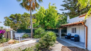 Un patio con mobiliario exterior, un edificio blanco con techo de tejas y diversas plantas.