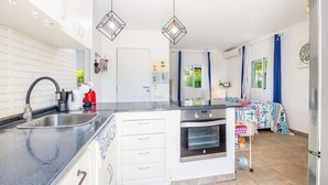 Una cocina moderna con horno empotrado, un lavamanos y una encimera. Hay una pequeña zona de comedor con una mesa y sillas.